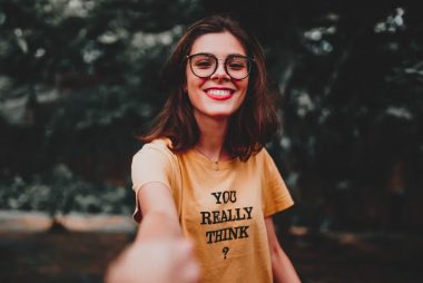 Happy woman in yellow shirt smiling broadly while enjoying the outdoors, wearing eyeglasses.